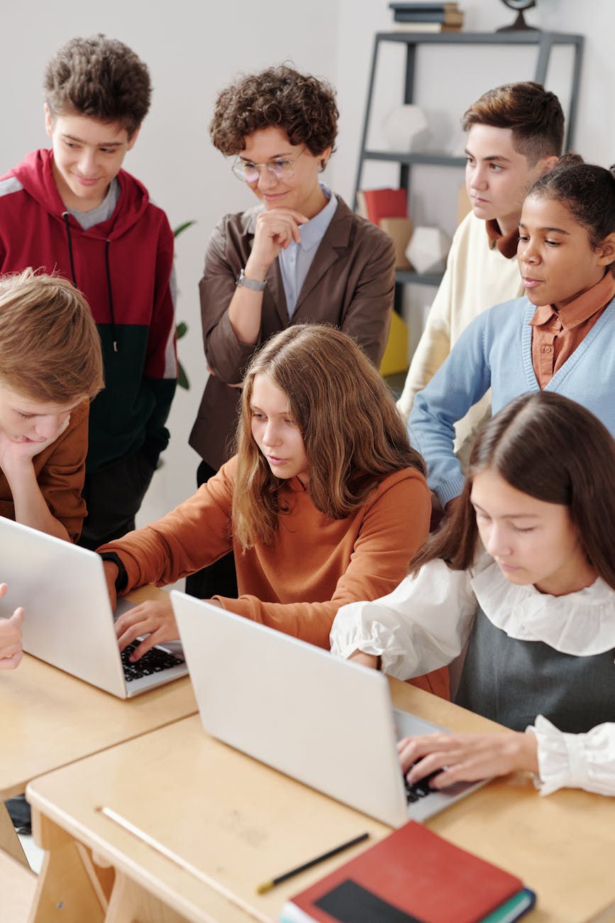 a two girls using laptop with classmates